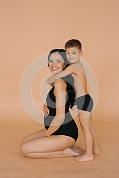 A happy young pregnant mother with her son on a beige background. The concept of a happy European or American family