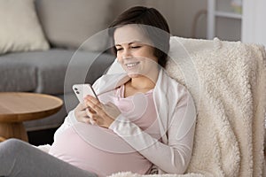 Happy young pregnant woman enjoying leisure at home, using smartphone