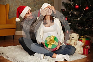 Happy young pregnant woman with her husband wearing christmas hats