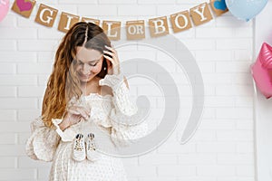 Happy young pregnant woman holding small baby shoes
