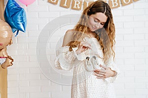 Happy young pregnant woman holding small baby shoes