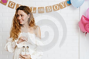 Happy young pregnant woman holding small baby shoes