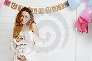 Happy young pregnant woman holding small baby shoes