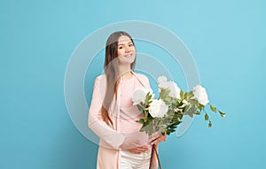 Happy young pregnant woman in pink t-shirt on blue background holding a bouquet of flowers