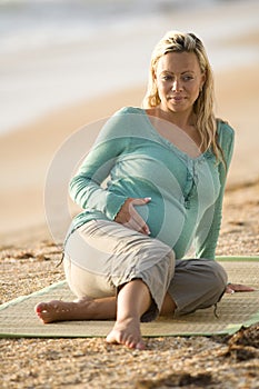 Happy young pregnant woman sitting on mat at beach