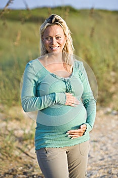 Happy young pregnant woman standing on beach