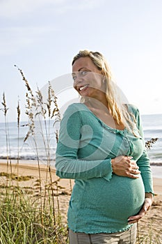 Happy young pregnant woman standing on beach