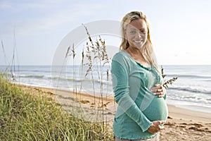 Happy young pregnant woman standing on beach