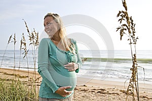 Happy young pregnant woman standing on beach