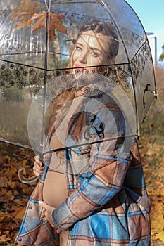 A happy young pregnant woman with an umbrella is waiting for her baby