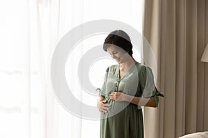 Happy young pregnant woman wearing stylish dress, touching big belly