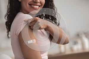 Happy young pretty african american female showing arm with band-aid after getting vaccination