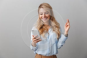 Happy young pretty blonde business woman posing  grey wall background using mobile phone