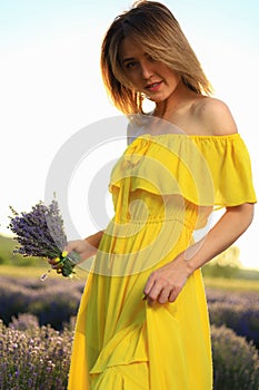 Happy young pretty modest smiling woman enjoying fresh air and aroma at sunset in a lavender field