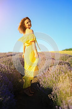 Happy young pretty modest smiling woman enjoying fresh air and aroma at sunset in a lavender field