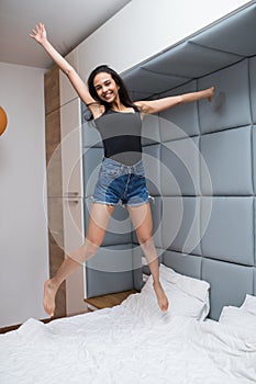 Happy young pretty woman jumping on her bed