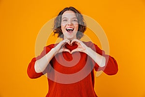 Happy young pretty woman posing isolated over yellow wall background showing heart gesture