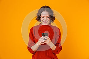 Happy young pretty woman posing isolated over yellow wall background using mobile phone