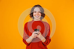 Happy young pretty woman posing isolated over yellow wall background using mobile phone