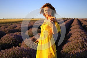 Happy young pretty woman walks at sunset in a lavender field with a bouquet in her hands and enjoys solitude with nature