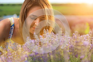 Happy young pretty woman walks at sunset in a lavender field and enjoys the smell of flowers and solitude with nature
