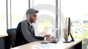 Happy young professional businessman sitting in office and working and looking at computer monitors and documents in the workplace