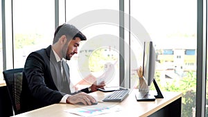 Happy young professional businessman sitting in office and working and looking at computer monitors and documents in the workplace