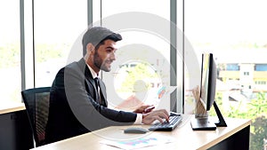 Happy young professional businessman sitting in office and working and looking at computer monitors and documents in the workplace