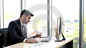 Happy young professional businessman sitting in office and working and looking at computer monitors and documents in the workplace