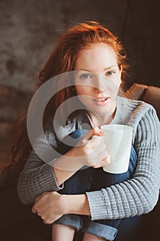 Happy young readhead woman drinking hot coffee or tea at home