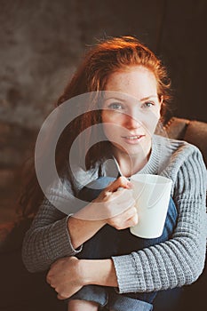 Happy young readhead woman drinking hot coffee or tea at home