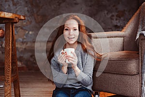 Happy young readhead woman drinking hot coffee or tea at home