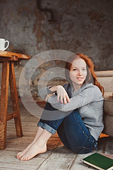 Happy young readhead woman drinking hot coffee or tea at home. Calm and cozy weekend in winter