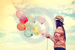 Happy young red hair woman holding colorful balloons and flying on clouds sky background.