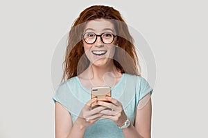 Happy young red-haired woman holding smartphone.
