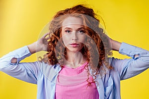 Happy young redhaired ginger woman with curly hairstyle pretty face wearing cotton pink shirt in studio yellow