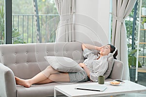 Happy young relaxed woman with headphones sitting on couch and listening to meditation music at leisure