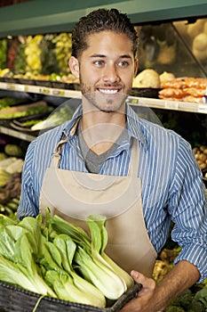 Happy young sales clerk holding bok choy in supermarket