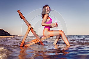 Happy young sexy woman in pink bikini posing with coctail on lounger beach. summer vacation concept