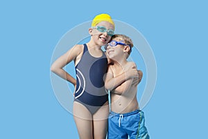 Happy young siblings in swimwear with arm around over blue background