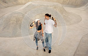 Happy young skateboarder couple relaxing after skate boarding exercise, posing in skate park, full length, free space
