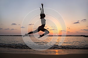 Happy young slender woman jumping and having fun at sunset on the beach by the sea