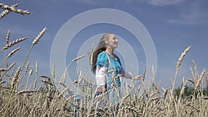 Happy young slender woman with a long fair hair in a blue dress rotates in the field of ripe wheat in summer sunny day