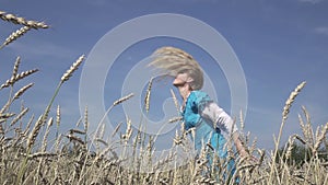 Happy young slender woman with a long fair hair in a blue dress rotates in the field of ripe wheat in summer sunny day.Slow motion