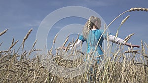 Happy young slender woman with a long fair hair in a blue dress rotates in the field of ripe wheat in summer sunny day.Slow motion