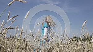 Happy young slender woman with a long fair hair in a blue dress rotates in the field of ripe wheat in summer sunny day.Slow motion