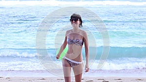 Happy young slim woman in swimsuit running on the beach side of ocean with green balloon with smile in slow motion