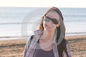 Happy young smiling brunette woman in sunglasses at sand beach by the sea.