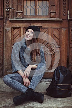 Happy young smiling hipster woman sitting near the door. Street fashion concept. Toned