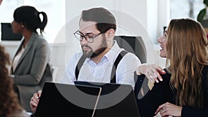 Happy young smiling male CEO manager discussing work with colleagues at team table meeting in modern light office.